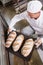 Baker taking tray of fresh bread out of oven