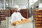 Baker in white uniform with trays of fresh bread costs in bakery.