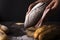 Baker woman holding rustic organic loaf of bread in hands - rural bakery. Natural light, moody still life.