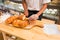 Bakery chef hand cutting fresh crusty loaf of bread on wooden bo