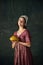 Bakery. Portrait of pretty young woman in image of renaissance maid holding freshly baked bread against vintage green