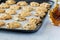 A baking sheet full of maple pecan cookies fresh out of the oven with a bottle of maple syrup on the side.