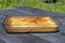 Baking tray with a delicious baked Charlotte stands on a wooden table, against the background of green vegetation