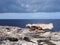 Balanced boulder on a rocky coastline scene with white stones against a calm blue sea and sky with sunlight and clouds