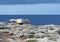 Balanced boulder on a rocky coastline scene with white stones against a calm blue sea and sky with sunlight and clouds