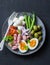 Balanced breakfast or snack - plate of canned tuna, green beans, mozzarella cheese, tomatoes, boiled egg, olives on a dark backgro