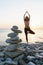 Balancing cairn of stones on the sea beach against the background of a woman out of focus performing the vrikshasana exercise