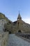 On the balcony of the monastery. Bell tower and cross on top. Carved railings, balconies and stairs. Stone walls, blue sky. David