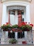 Balcony with white window frames and red flowers in the planters hanging on cast iron decorative railings