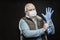 A bald adult masked man puts on blue medical gloves on his hands. Precautions during the coronavirus pandemic. Black background