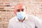 Bald adult mature man in medical mask with emotions against brick wall