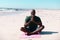 Bald african american senior man meditating while sitting cross legged on sandy beach in summer