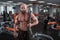 A bald, bearded bodybuilder with large relief muscles holds a heavy thick chain in his hands. Bright gym