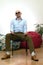 Bald bearded brutal macho or gangster man in sunglasses sitting on chair looking at camera. Confidence, individuality, masculinity