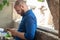 Bald bearded man wearing a blue shirt with dots leaning on a stone wall, holding a phone and looking at it