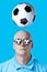 Bald brutal man in dark round glasses with highlights. A football hovered overhead. On a blue background