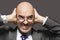 Bald Businessman With Hands Over Ears Looking Sideways