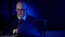 Bald businessman, in a suit and glasses, middle-aged, sitting in the dark behind a laptop, much surprised and frightened