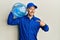 Bald courier man with beard holding a gallon bottle of water for delivery pointing finger to one self smiling happy and proud