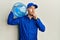 Bald courier man with beard holding a gallon bottle of water for delivery serious face thinking about question with hand on chin,