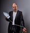 Bald fun gloomy aggressive comic business man holding the home iron and wanting to hit in suit on grey background. Closeup