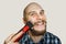 Bald guy with a beard and a clipper in his hands, shaving himself in the morning at home on a colored background