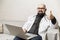 A bald male doctor in a white coat with glasses sits with a laptop on the couch. Online consultations. Quarantine during the