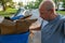 Bald male senior citizen stands in the street looking into his recycling bin at its cardboard contents