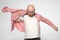 Bald man with glasses putting on a coral-colored shirt, he is preparing for some event and is very serious.