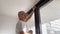 Bald man in middle-aged glasses is twisting screws for cornices on the window in the room, the concept of male homework, repair,