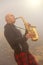 A bald man plays on a gold alto saxophone in the nature, against