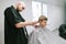 Bald man professional barber cuts the client`s hair with a clipper in the hands, looks at the young man`s head. A young man cuts