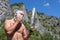 bald man shaves cheek with long knife phone on natural background. Morning on hike. Destination experience lifestyle concept