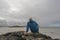 Bald man sitting on a rock by the ocean looking water. Beautiful nature scenery in the background. West coast of Ireland. Back to