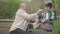 The bald mature man sitting in the park on the bench with a book, talking with his grandson. Then people shake hands and