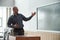 Bald mature teacher looking and pointing at notes on blackboard