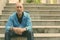 Bald senior man leaning arms on knees while sitting on the staircase in Bangkok Thailand