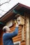 Bald senior with a mustache attaches birdhouse to the barn