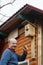 Bald senior with a mustache attaches birdhouse to the barn