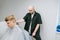 Bald serious professional haircutter cuts a young man with a clipper in his hands, looks intently at his head against a light wall