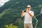 A bald tourist in sunglasses at a halt takes a picture on his camera. Against the backdrop of green mountains and a