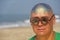 A bald and unusual young man, a freak, with a shiny bald head and round wooden glasses on the background of the beach and the sea