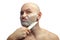 A bald white man shaves his stubble with a shiny kitchen knife. A man's face with shaving foam.