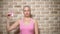 Bald woman Survivor after cancer proudly holds a pink ribbon in her hands against a brick wall.