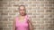 Bald woman Survivor after cancer proudly holds a pink ribbon in her hands against a brick wall.