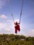 Bali swing trend. Caucasian woman in long red dress swinging in the jungle rainforest. Vacation in Asia. Travel lifestyle. Blue