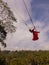 Bali swing trend. Caucasian woman in long red dress swinging in the jungle rainforest. Vacation in Asia. Travel lifestyle. Blue