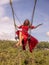 Bali swing trend. Caucasian woman in long red dress swinging in the jungle rainforest. Vacation in Asia. Travel lifestyle. Blue