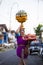 Balinese woman with cild loads the offering of food in wooden jar on her head