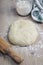 ball of dough on a wooden table surrounded by a rolling pin, a jar with flour and a kitchen rag